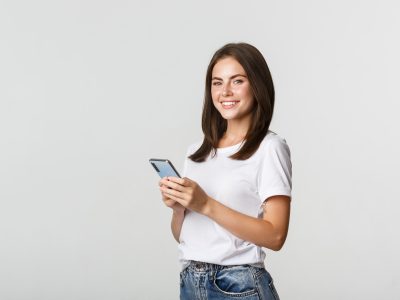 Attractive young brunette woman using mobile phone and smiling at camera.