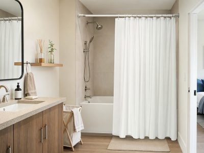 Banheiro organizado com cortina para box branca, varão extensível e cesto dobrável, com aromatizador em prateleira.