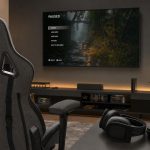 Setup gamer com cadeira cinza e preta, headset e controle ao lado da TV, ambiente confortável para jogar sem incomodar em casa