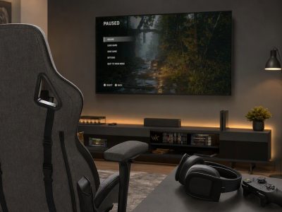 Setup gamer com cadeira cinza e preta, headset e controle ao lado da TV, ambiente confortável para jogar sem incomodar em casa