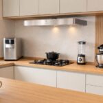 Cozinha moderna organizada com coifa, purificador, liquidificador, batedeira, cafeteira, mixer e processador dispostos na bancada.