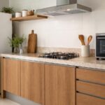 Cozinha moderna com geladeira branca, cooktop e forno de bancada sobre uma bancada de pedra, iluminada por luz natural.