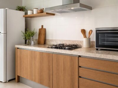 Cozinha moderna com geladeira branca, cooktop e forno de bancada sobre uma bancada de pedra, iluminada por luz natural.