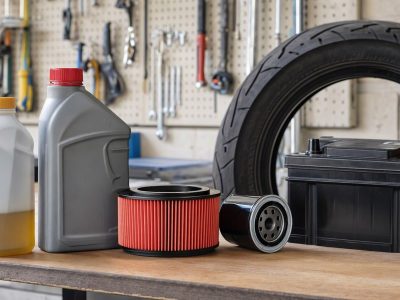 Bancada de garagem com fluido de freio, ATF, filtros de moto, pneu e bateria dispostos para revisão automotiva.