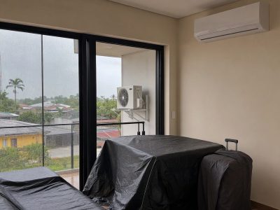Sala com ar-condicionado split instalado e unidade externa em suporte, móveis protegidos e mala com capa, cenário de instalação na Região Norte.