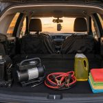 Kit de emergência automotivo organizado no porta-malas com macaco garrafa, compressor, cabo de chupeta, shampoo e microfibra, mais capa de banco e suporte de celular instalados.
