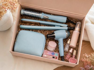 Flat lay de kits de beleza com ferramentas de cabelo, sérum, hidratante, protetor solar em spray e nécessaire, em caixa de presente.