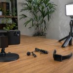 Setup simples para gravar vídeos com celular, microfone de lapela, luminária e smartwatch em mesa.