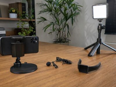 Setup simples para gravar vídeos com celular, microfone de lapela, luminária e smartwatch em mesa.