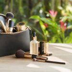 Sérum facial e itens de maquiagem organizados dentro de uma bolsa elegante, em ambiente iluminado, clima tropical ao fundo.
