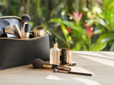 Sérum facial e itens de maquiagem organizados dentro de uma bolsa elegante, em ambiente iluminado, clima tropical ao fundo.