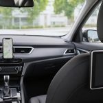Suporte de celular no painel com navegação e tablet fixado no banco traseiro, interior de carro organizado.