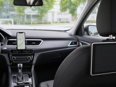 Suporte de celular no painel com navegação e tablet fixado no banco traseiro, interior de carro organizado.