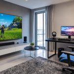 Sala com TV grande e mesa com monitor gamer lado a lado, mostrando dois setups de jogo possíveis.