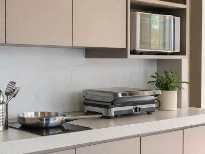 Cozinha organizada com porta-talheres inox, frigideira, micro-ondas e churrasqueira elétrica sobre a bancada.