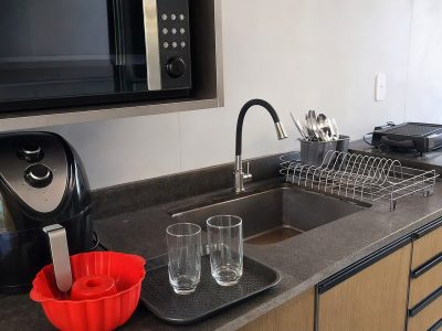 Cozinha moderna com micro-ondas, air fryer com forma de silicone, escorredor de talheres e copos de vidro sobre a bancada, pronta para refeições rápidas.
