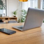 Smartphone e notebook sobre mesa de madeira em ambiente interno iluminado, representando compras online sem pessoas.
