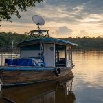 Barco de madeira no rio amazônico com antena de internet satelital instalada no convés.