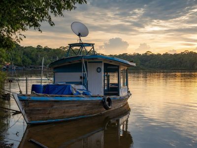 Barco de madeira no rio amazônico com antena de internet satelital instalada no convés.