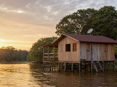 Antena de internet via satélite instalada no telhado de casa ribeirinha na Amazônia, ao entardecer.