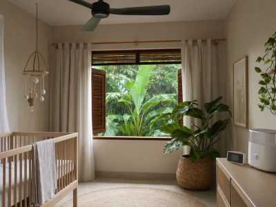 Quarto de bebê arejado com berço, roupa de cama leve, relógio de mesa e umidificador, em clima tropical.